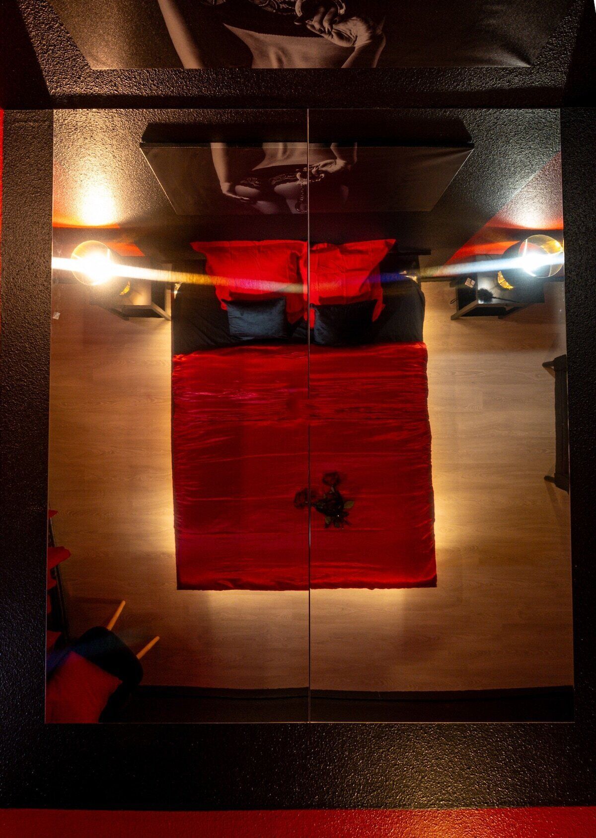 Een kamer met een houten vloer, een rood beddegoed en twee wandlampen.