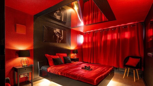 Une chambre moderne aux tons rouges, comprenant un grand lit, une table de chevet et une chaise.