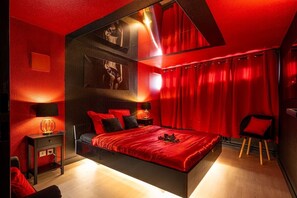 Une chambre moderne aux tons rouges, comprenant un grand lit, une table de chevet et une chaise.