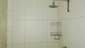 A shower area with a handheld showerhead, a metal shelf, and a wall-mounted faucet.