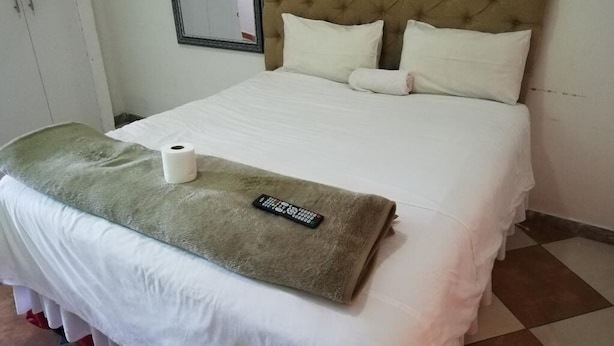 A neatly made bed with a remote control, a roll of toilet paper, and a green towel on the bed.