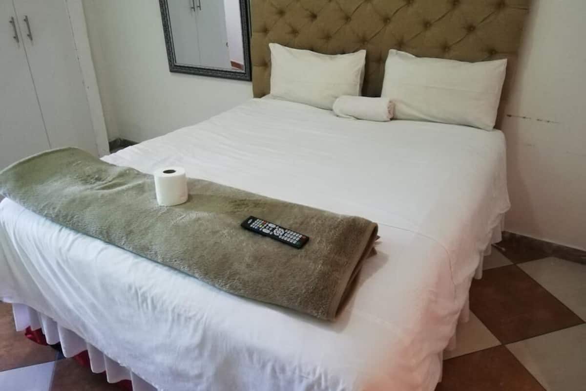 Un lit bien fait, avec une télécommande, un rouleau de papier toilette et une serviette verte posée sur le lit.