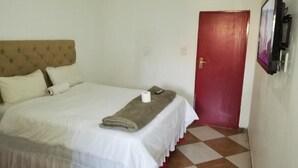 A hotel room with a bed, a red door, and a wall-mounted TV.