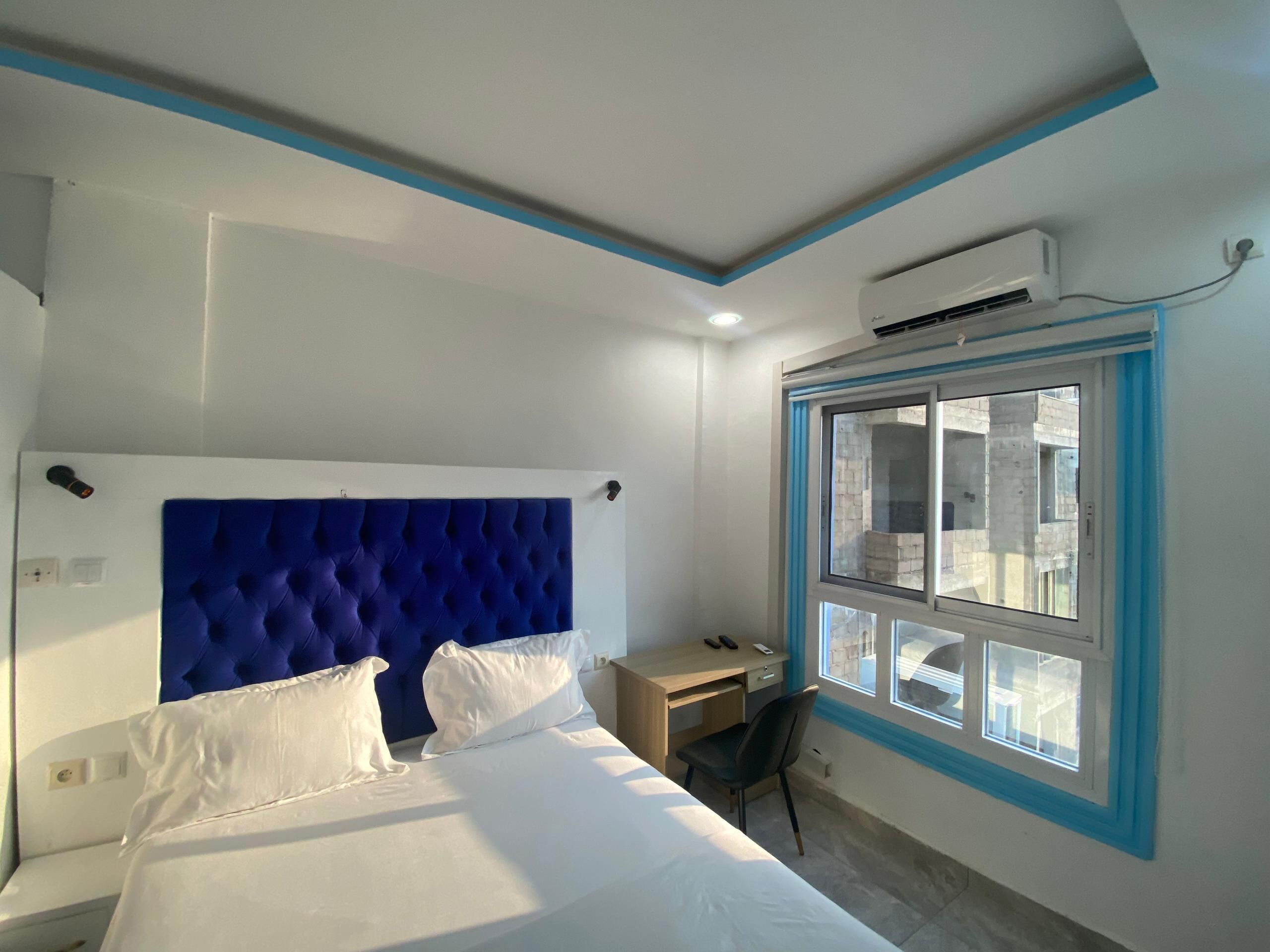A bedroom with a large bed, a desk, and a window with a view of buildings.