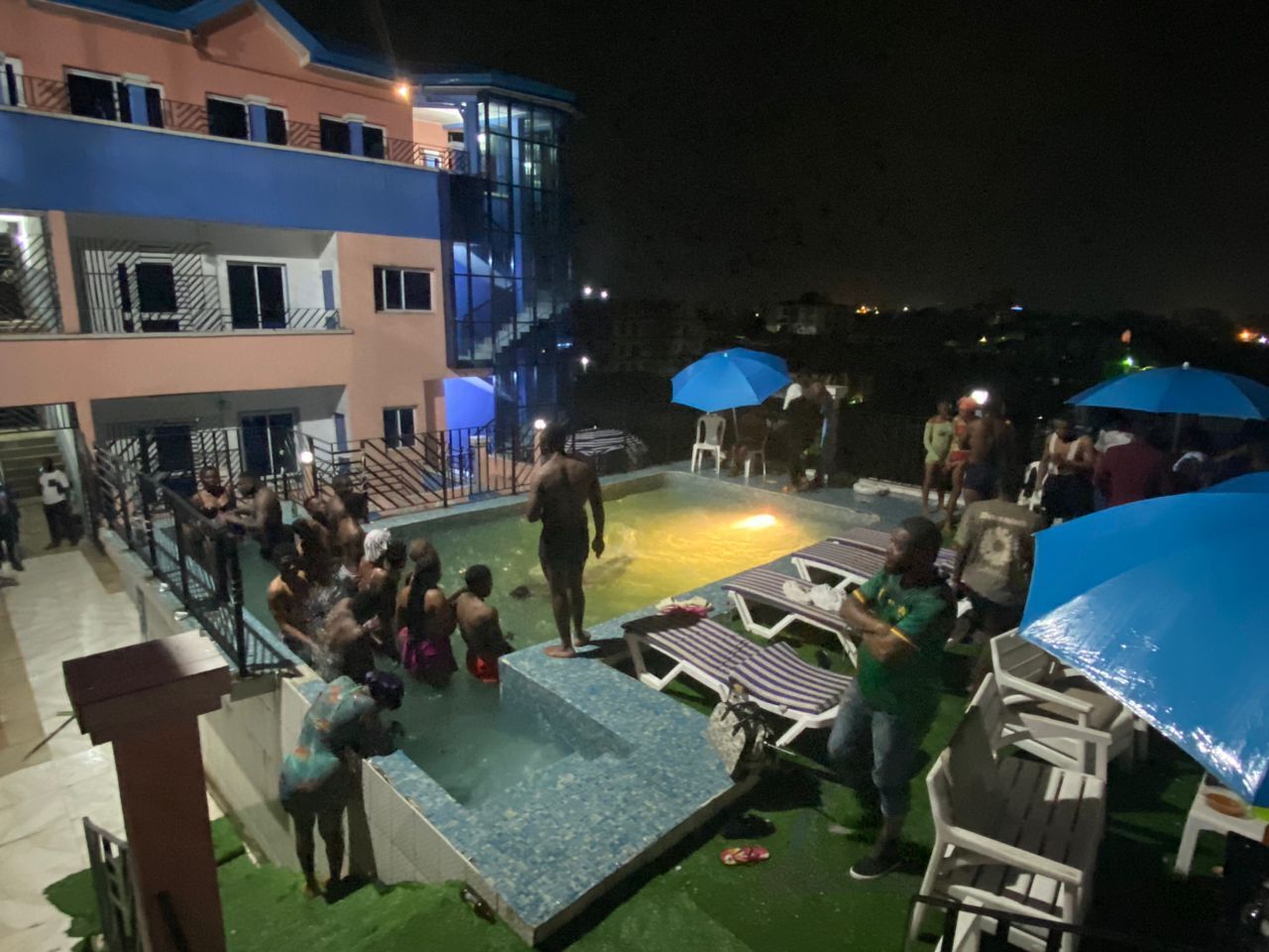 Zona de piscina en la azotea con sillones de descanso y sombrillas, rodeada de edificios.