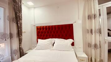 Habitación de hotel con cabecera tapizada en rojo, ropa de cama blanca y puerta con vistas.