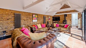 A spacious living room with a brick wall, a fireplace, and a large window. - The Willows -  a holiday let by Bloom Stays that sleeps 8 guests  in 4 bedrooms (Ash)