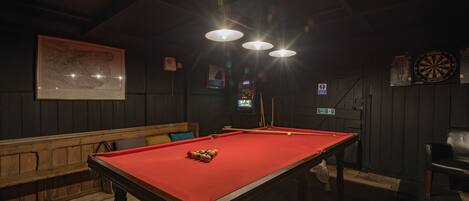 A billiards table with a red cloth, a wooden bench, and a dartboard on the wall.