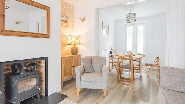 Un salon chaleureux avec une cheminée, un fauteuil confortable, une table à manger avec des chaises et un buffet en bois.