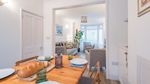 Un coin repas avec une table en bois, des chaises et une miche de pain. On aperçoit un canapé et une lampe au fond.