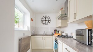 Une cuisine moderne avec des meubles blancs, un plan de travail en bois et une grande horloge murale.