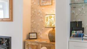 Un salon chaleureux avec un meuble en bois, une lampe décorée d’un motif représentant un hippocampe, un tableau encadré et une bibliothèque contenant des livres et un objet décoratif.