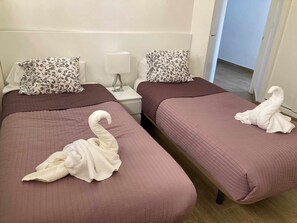 Deux lits jumeaux, chacun agrémenté d’oreillers assortis à motifs floraux et d’une serviette décorative en forme de cygne.