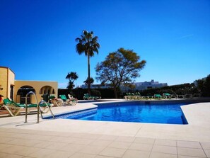 Une piscine avec des chaises longues et des palmiers.