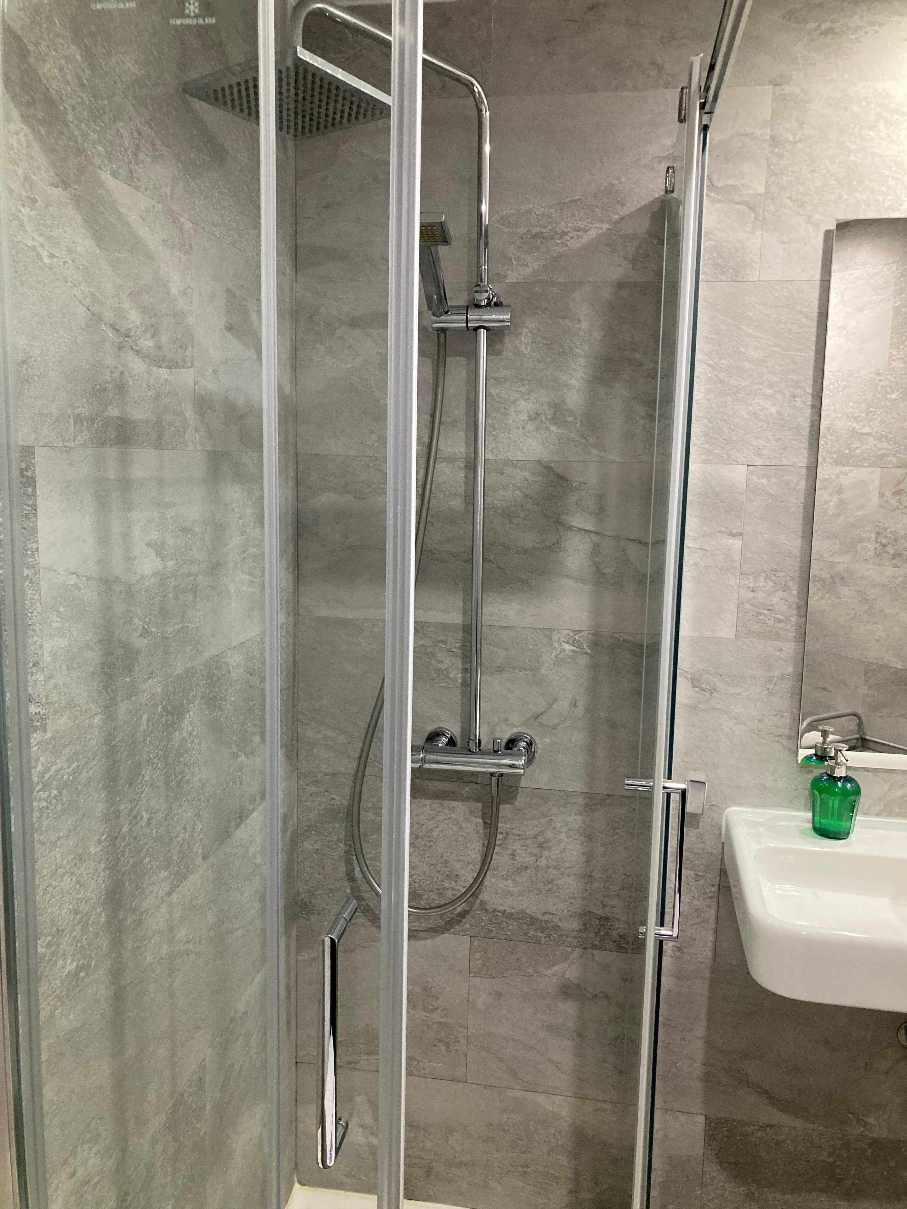 Ducha con mampara de vidrio, cabezal de ducha manual y grifo empotrado.