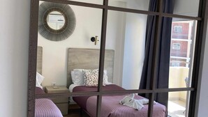 A hotel room with two beds, a large mirror, a round wall mirror, a bedside table, and a view of the outside. - Luxury Apartment in Club Playa Flores (Torremolinos)