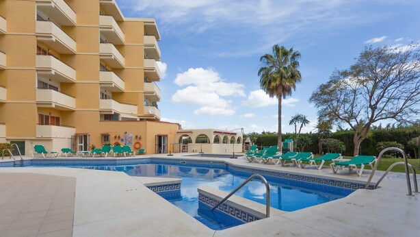 A hotel pool area with a clear blue pool, green lounge chairs, and a palm tree. - Luxury Apartment in Club Playa Flores (Torremolinos)
