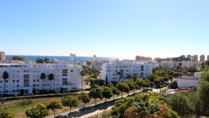 A coastal cityscape with modern white buildings, a clear blue sky, and a view of the sea. - Luxury Apartment in Club Playa Flores (Torremolinos)