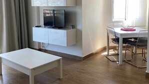 A modern living room with a flat-screen TV, a white dining table, and a bench. - Luxury Apartment in Club Playa Flores (Torremolinos)
