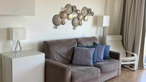 Un salon moderne avec un canapé marron, des coussins à motifs, une table d’appoint blanche, une lampe sur pied et un élément décoratif mural.