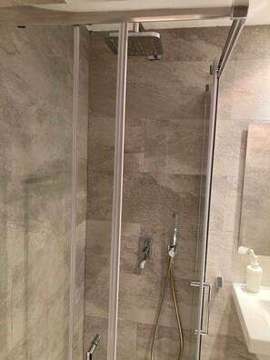 Une douche fermée par des parois en verre, dotée d’un pommeau de douche à main et d’un robinet mural.