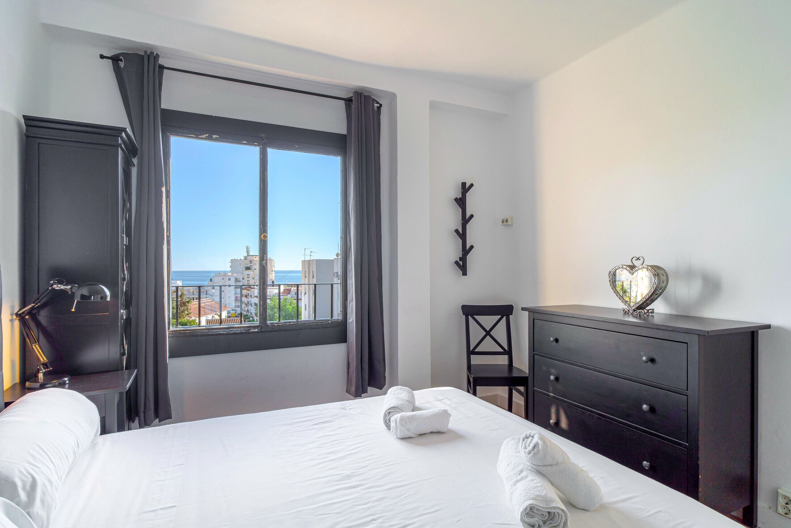 A hotel room with a bed, a desk, a chair, a dresser, and a view of the city.