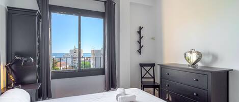 A hotel room with a bed, a desk, a chair, a dresser, and a view of the city.