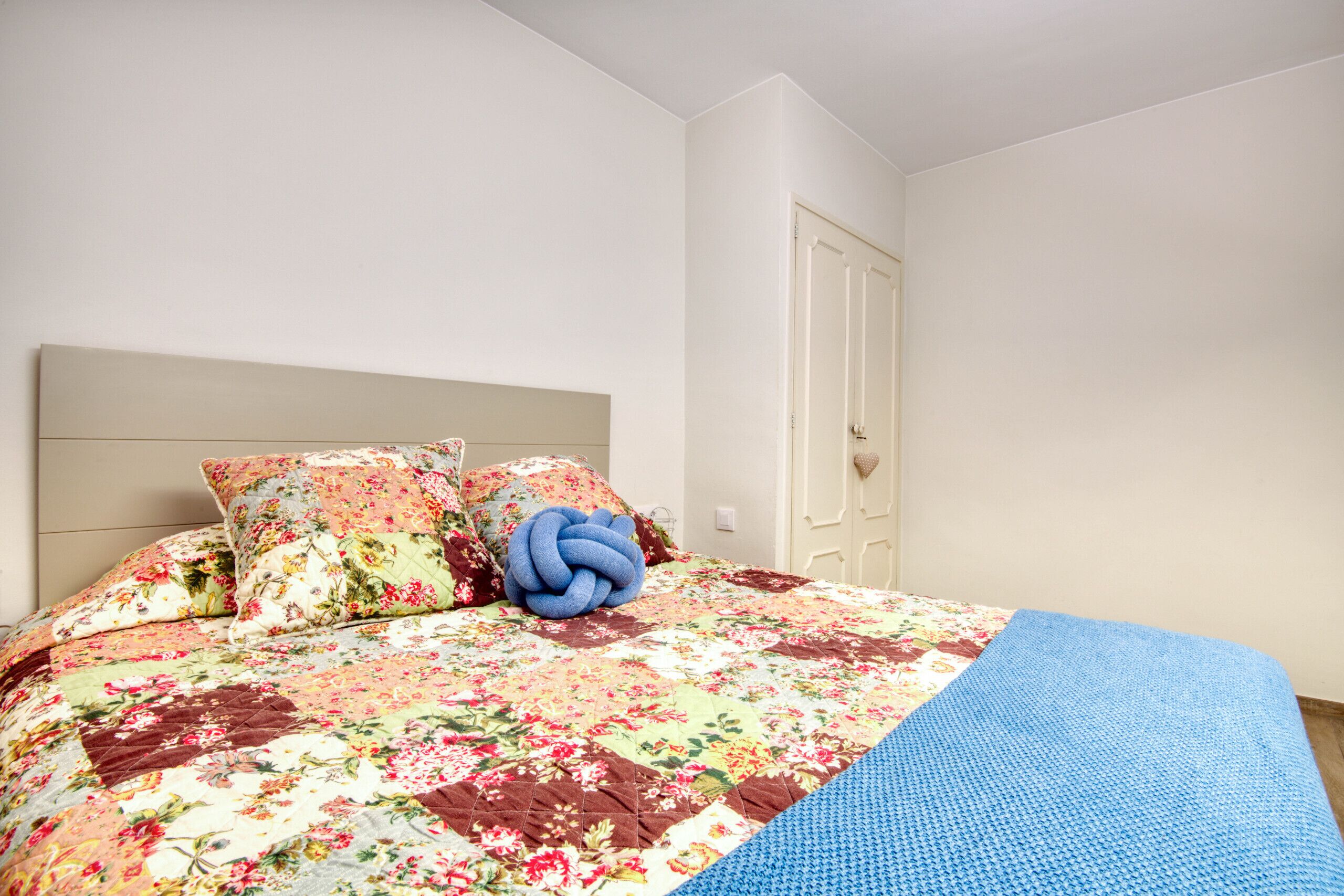 A neatly made bed with floral bedding and a blue throw blanket.