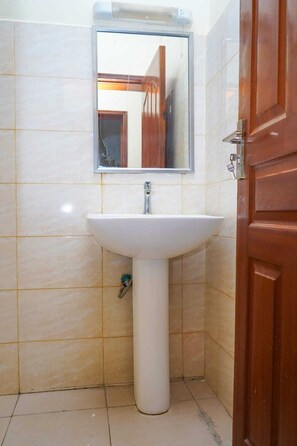 Een badkamer met een wit wastafeltje, een spiegel erboven en een houten deur.