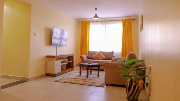 A living room with a sofa, a coffee table, a TV, and a plant. - Lux Suites Greatwall Getaway Apartments (Athi River)