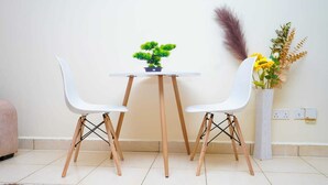 A small dining area with two white chairs, a wooden table, and a potted plant. - Lux Suites Greatwall Getaway Apartments (Athi River)
