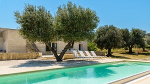 A swimming pool with lounge chairs, a tree, and a building with a stone facade. - Villa La Guaceta by Wonderful Italy (Carovigno)