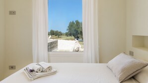 A bedroom with a bed, a window with curtains, and a view of a landscape. - Villa La Guaceta by Wonderful Italy (Carovigno)