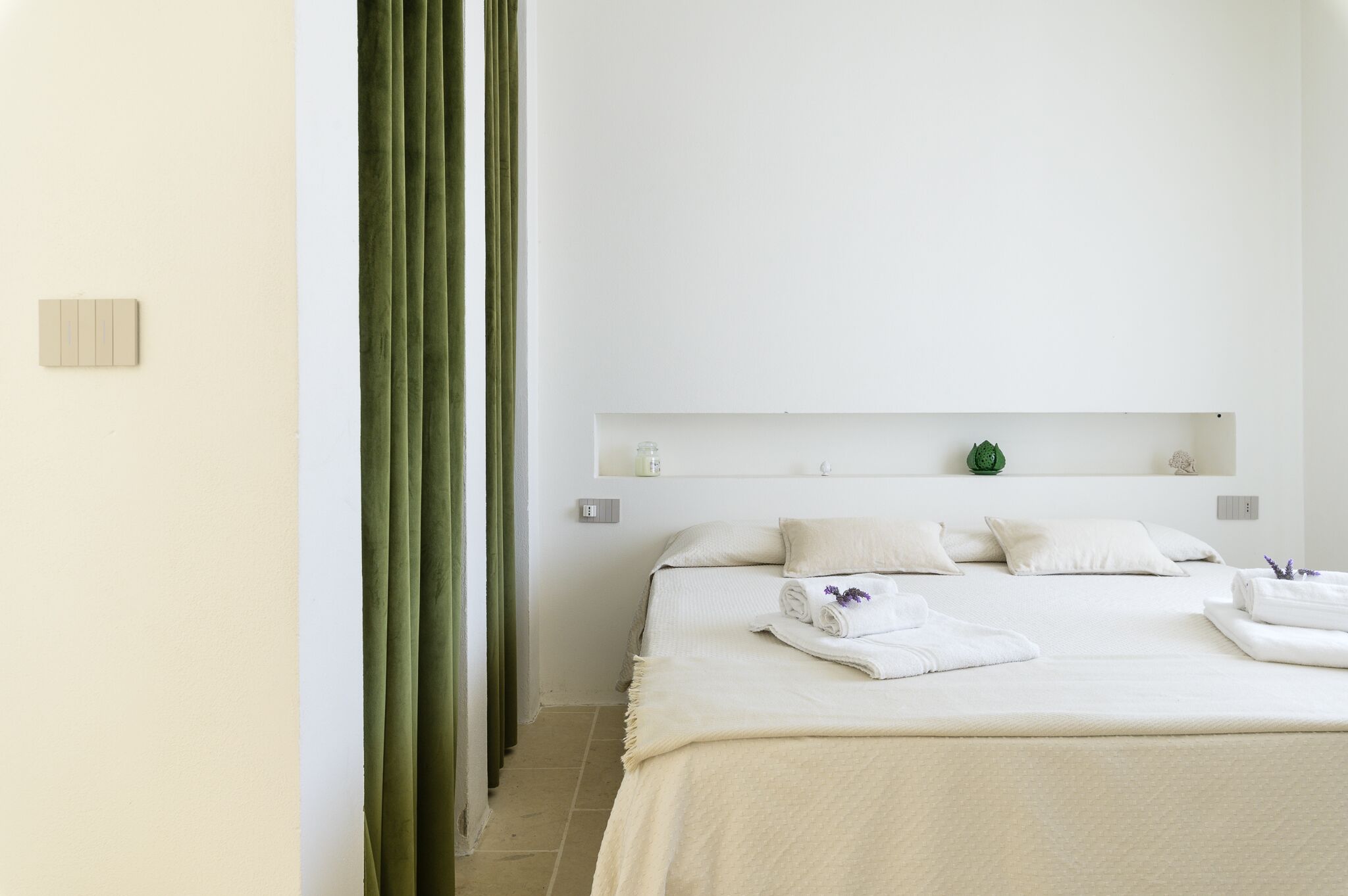 Camera d'albergo dal design minimalista, con un letto, una tenda verde e uno scaffale con articoli da toilette.