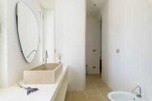 Un baño moderno con un lavabo color beige, un espejo grande y un lavamanos blanco sobre pedestal.