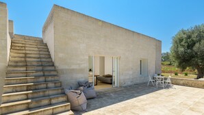 A modern building with a staircase leading to a glass door entrance, a patio area with outdoor furniture, and a view of the surrounding landscape. - Villa La Guaceta by Wonderful Italy (Carovigno)