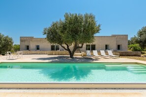 Un edificio moderno con piscina, sillas de descanso y un árbol en primer plano.
