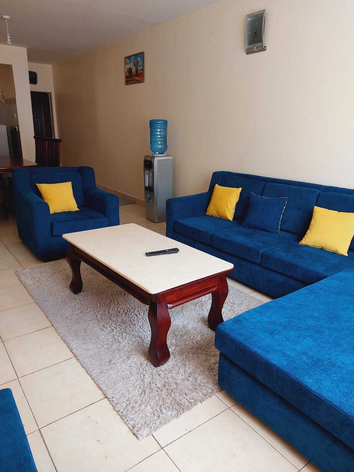 A living room with a blue sofa set, a wooden coffee table, and a water dispenser.