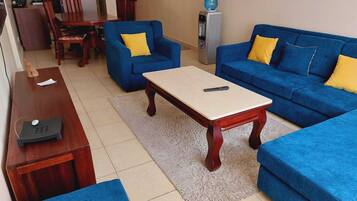 Una sala de estar con sofá, sillón, mesa de centro y una mesita de madera con un control remoto.
