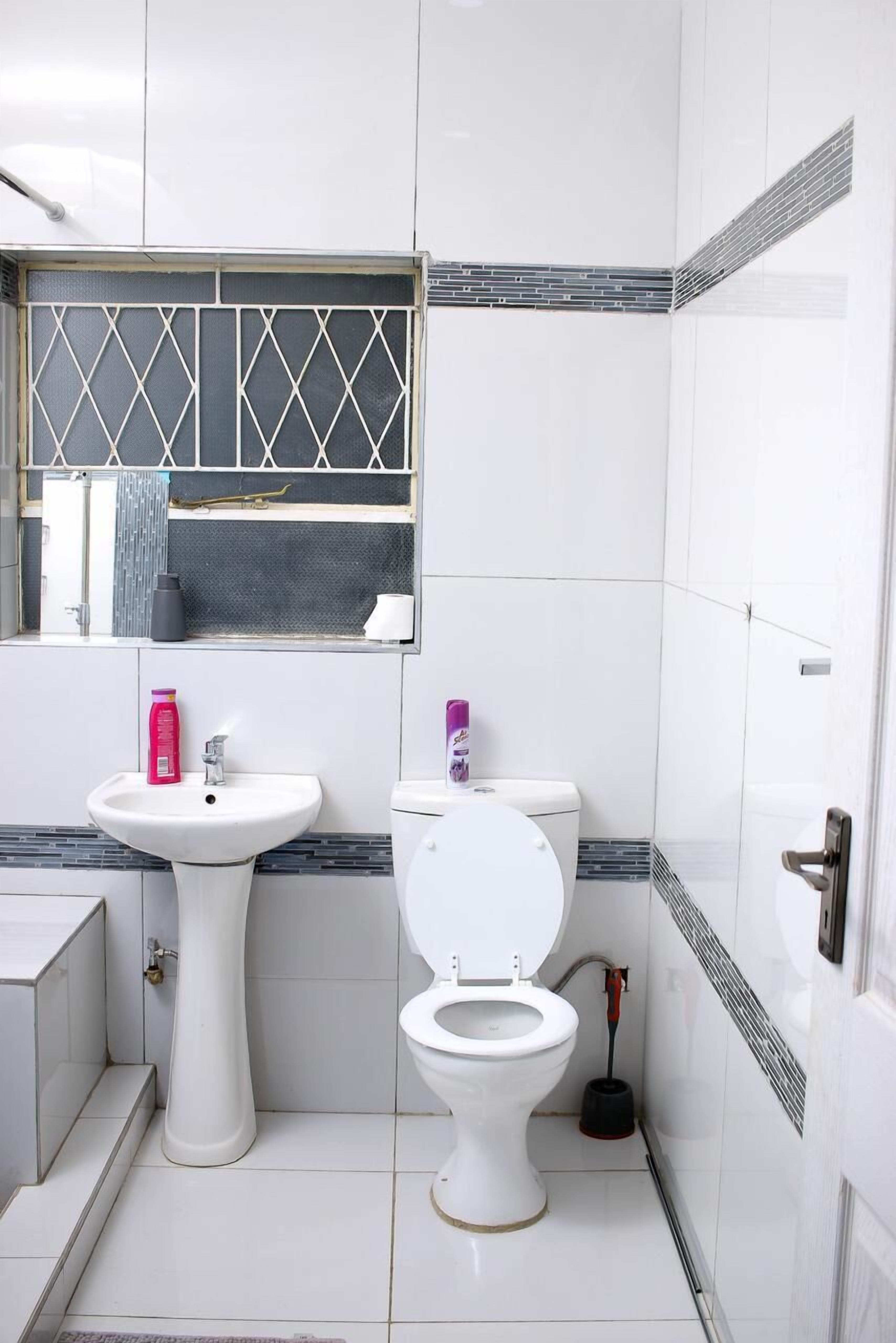 Un baño pequeño y limpio con un lavamanos, inodoro y ventana con celosía de metal.