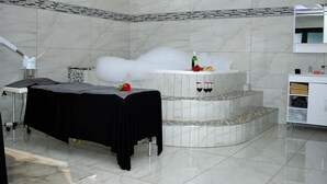 A spa room with a massage table, a small seating area, and a counter with a bottle and glasses. - Semeni Asante Getaway (Johannesburg South)