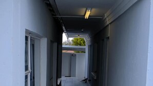 A narrow corridor with tiled flooring and white walls, leading to a gated area. - Semeni Asante Getaway (Johannesburg South)