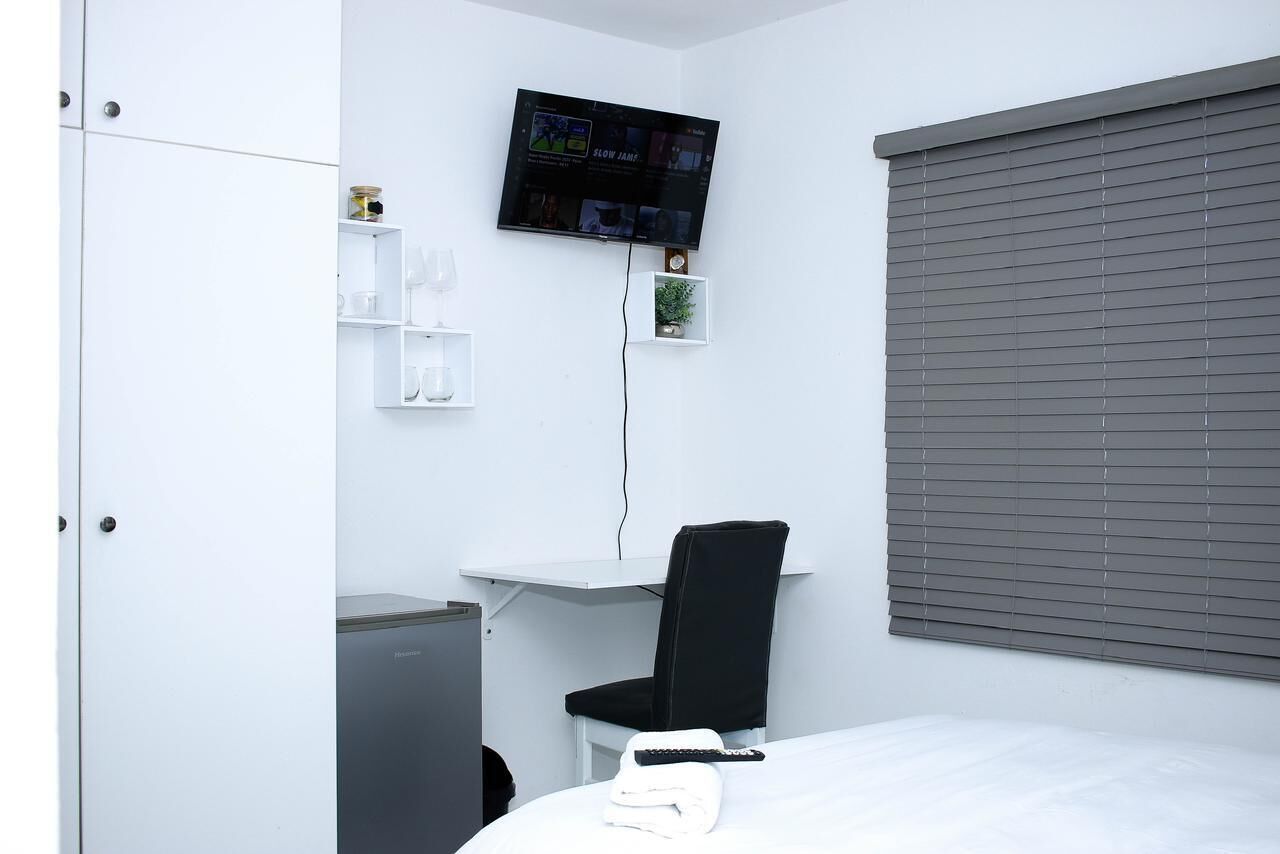 Una habitación de hotel moderna con cama, escritorio, silla, televisor y ventana con persianas.