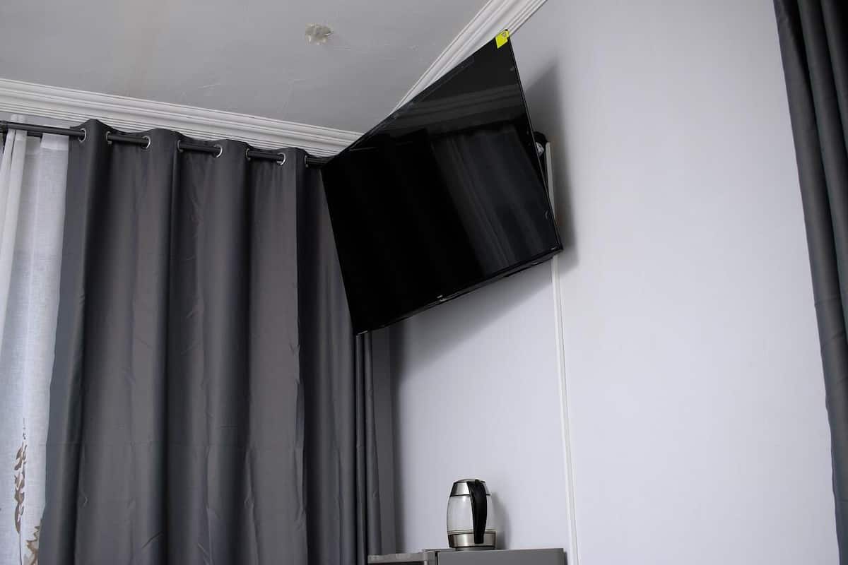 Habitación con televisión de pantalla plana montada en la pared, cafetera sobre una mesa y cortinas grises.