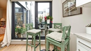 Un balcón con puerta de vidrio, una mesa con sillas y plantas en macetas.
