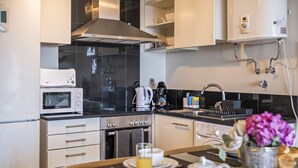 A modern kitchen with a microwave, stove, and coffee maker. There is a sink with a faucet, and a vase with flowers on the counter.