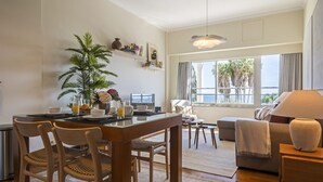 A modern living room with a dining area, large windows with a view of palm trees, and a cozy seating arrangement.