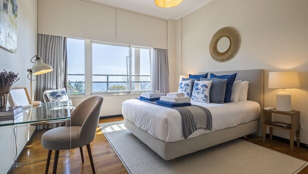 A modern bedroom with a large bed, a desk, a chair, and a view of the outdoors.
