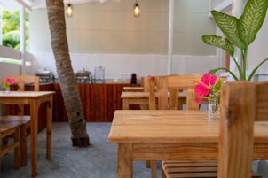 A wooden table with a vase of pink flowers, a wooden chair, and a large green plant in a restaurant setting.