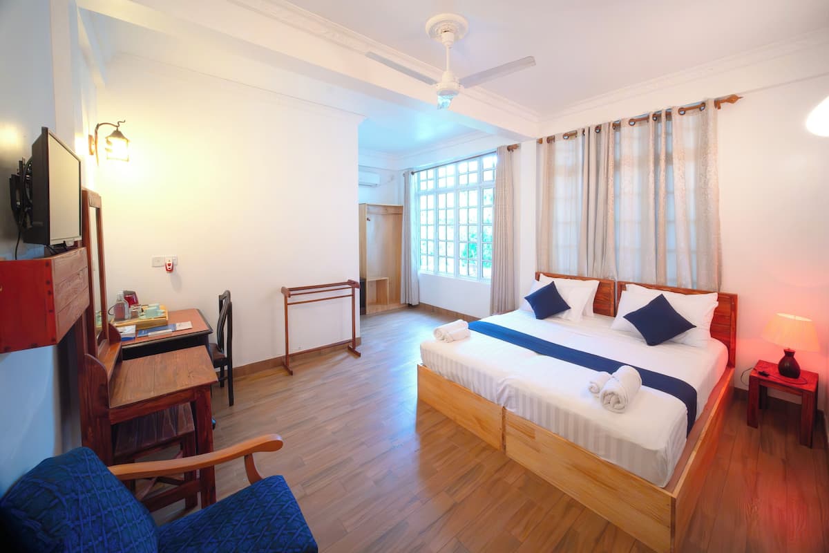 A bedroom with a bed, a desk, a chair, a ceiling fan, and a window with curtains.